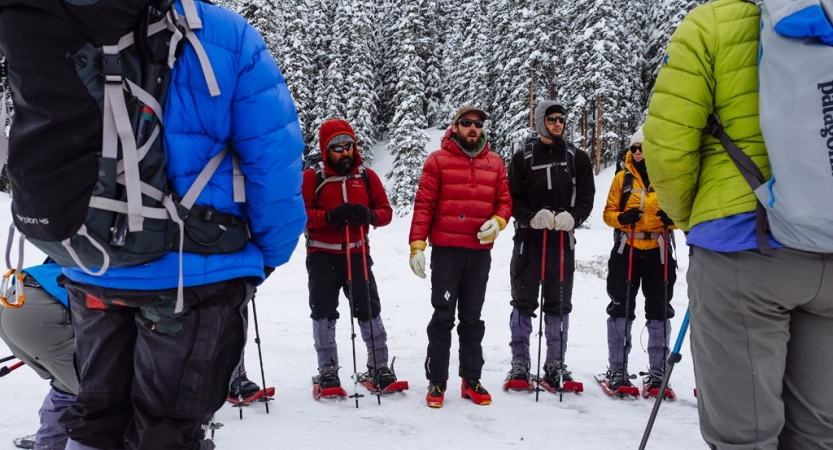 A group of people wearing winter gear stand in a circle in a snowy landscape.